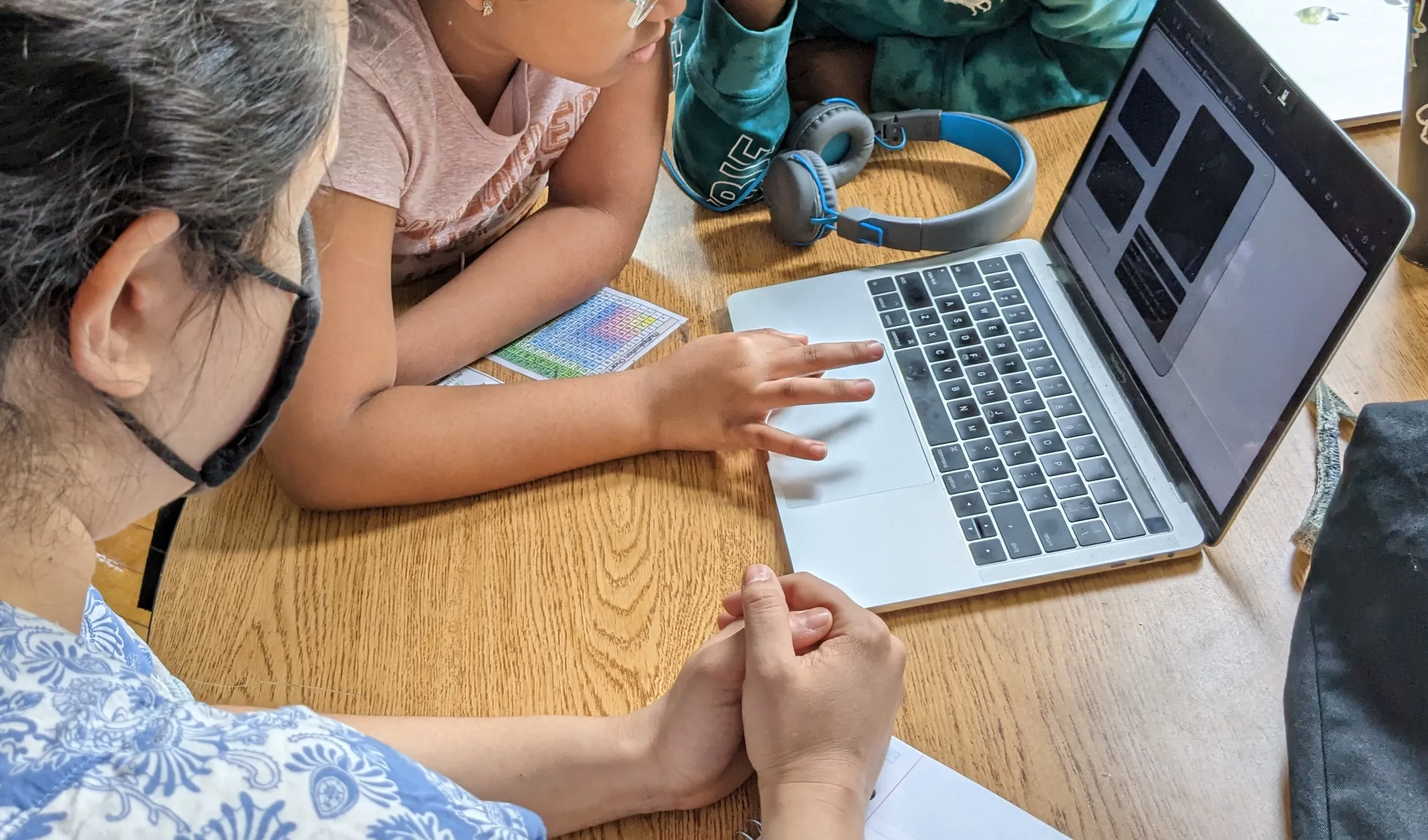 A child leans over a desk to play Project Space Watch on a computer, while a girl sitting nearby looks on."